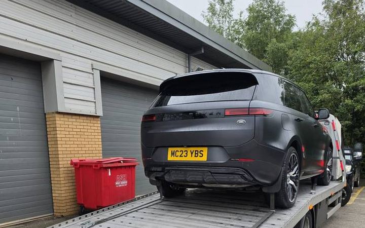 Black Ford electric vehicle on recovery flatbed at residential house driveway