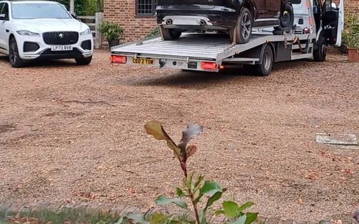 Black Porsche SUV and white Jaguar luxury vehicles on recovery flatbed