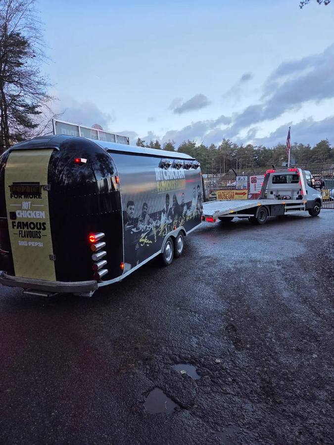 Black food service trailer with branding transported on recovery truck