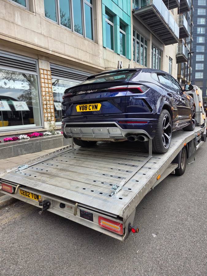 Black Lamborghini Urus luxury SUV on recovery truck flatbed