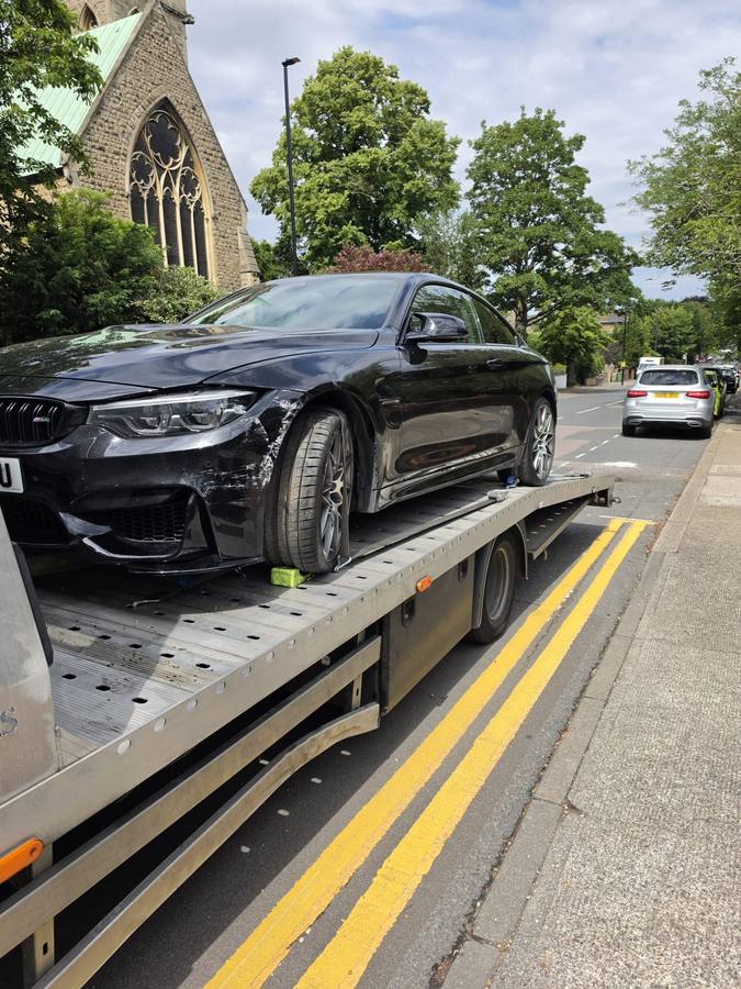 Black BMW SUV with left-side collision damage on flatbed