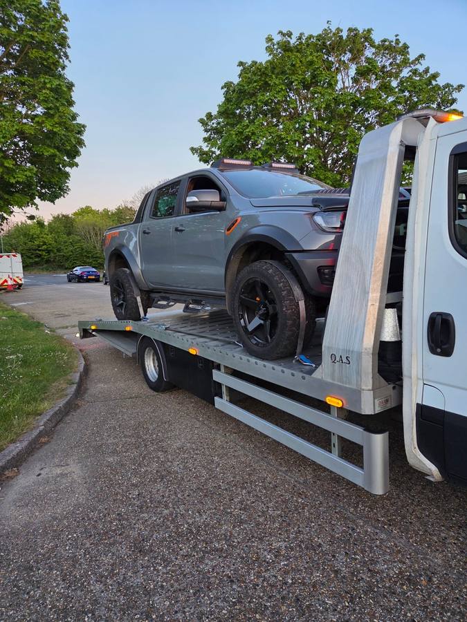 Gray Mitsubishi pickup truck loaded on recovery truck flatbed