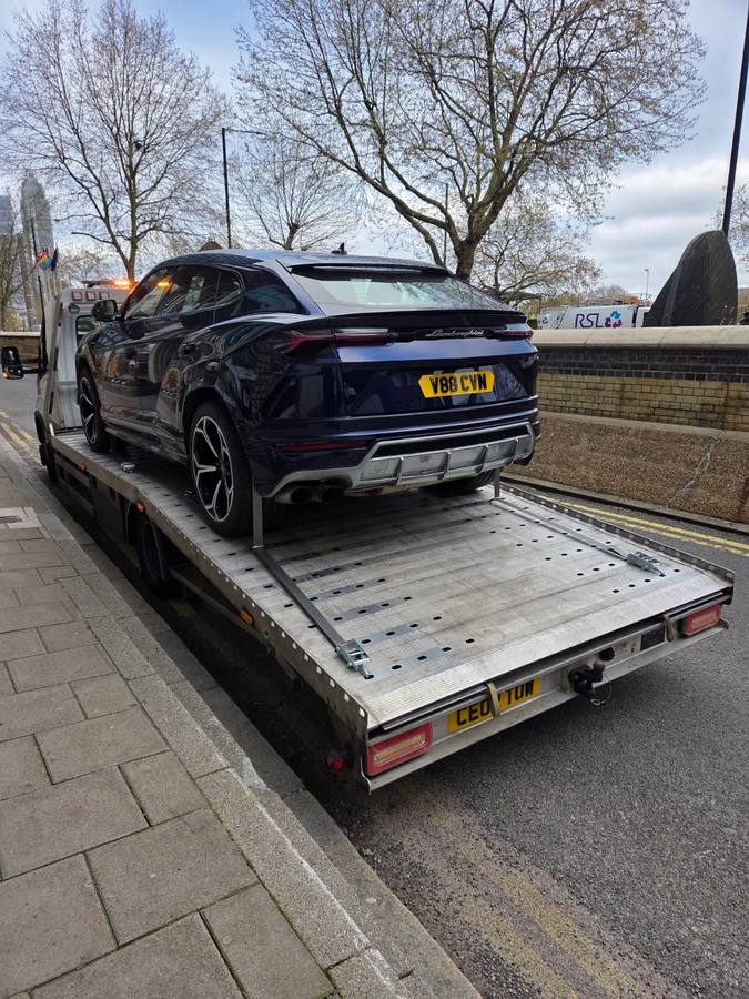 Black Lamborghini Urus SUV loaded on recovery truck flatbed