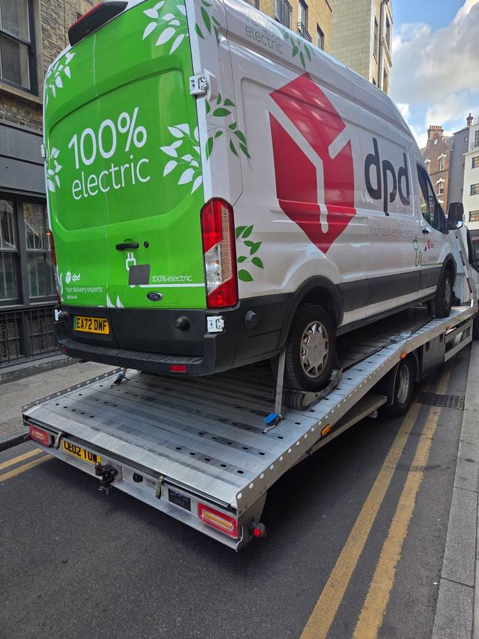 Green and white electric DPD delivery van loaded on flatbed in London street