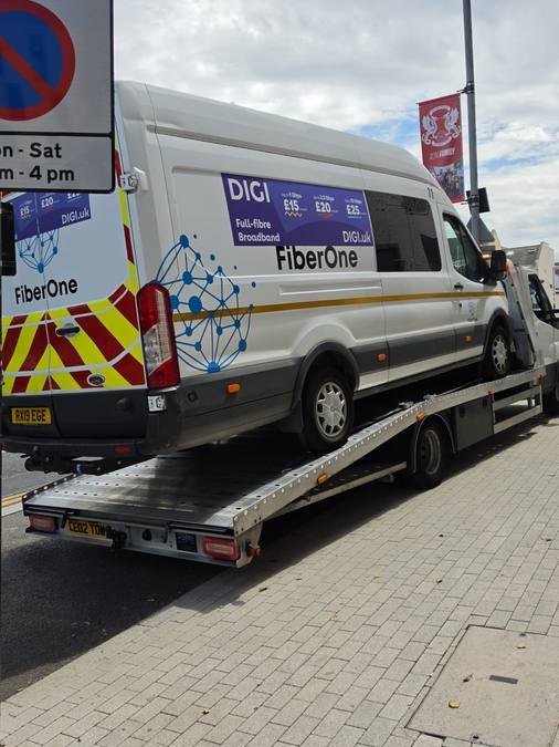 White FiberOne branded commercial van secured on recovery flatbed outdoors
