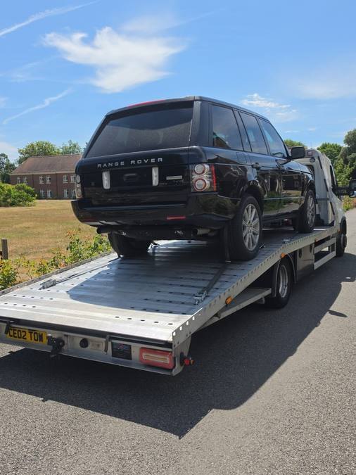 Black Range Rover SUV loaded on flatbed at residential street location