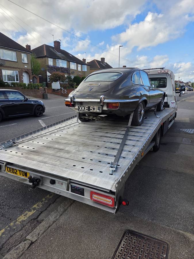 Dark vintage car transported on flatbed in London street with other vehicles