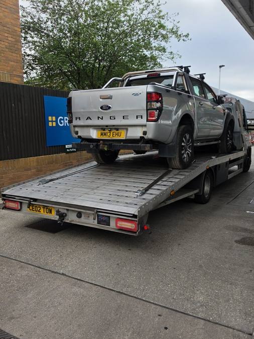 White Ford Ranger pickup truck loaded on recovery flatbed outside warehouse