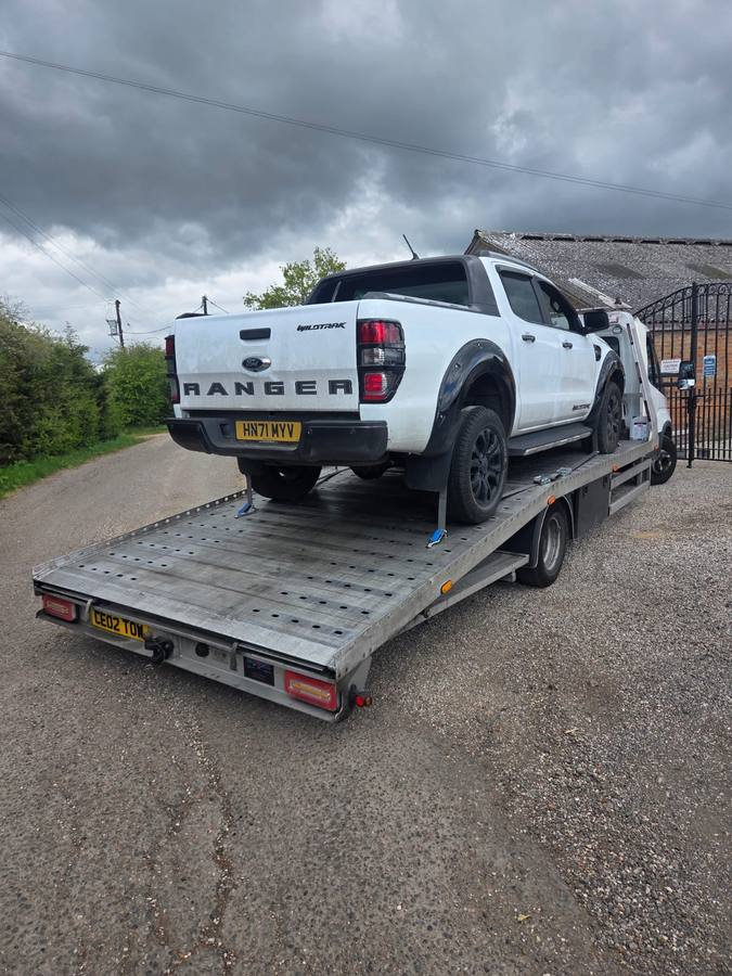 White Ford Ranger pickup truck on recovery flatbed at gravel yard location