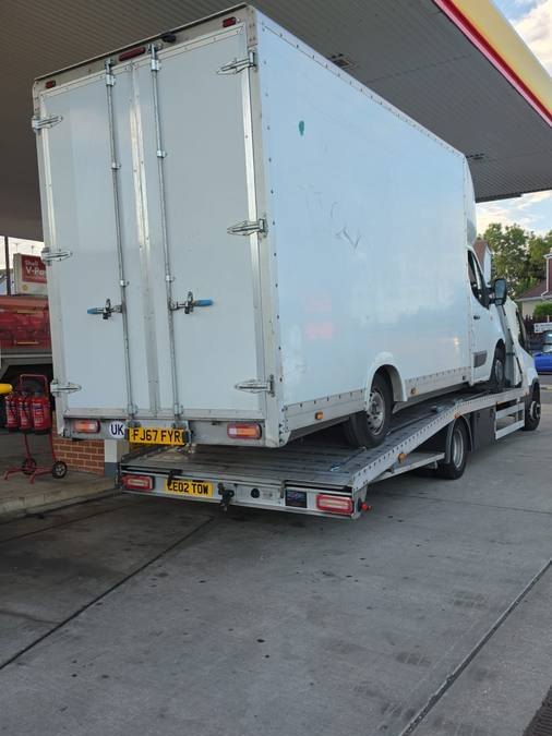 White commercial box van secured on flatbed at petrol station forecourt