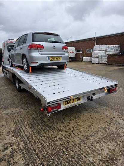 Grey Volkswagen Golf transported on recovery flatbed at warehouse facility