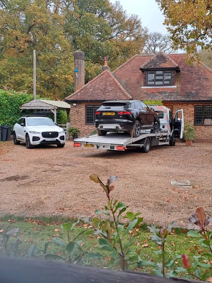 Black Porsche SUV and white Jaguar luxury vehicles on recovery flatbed