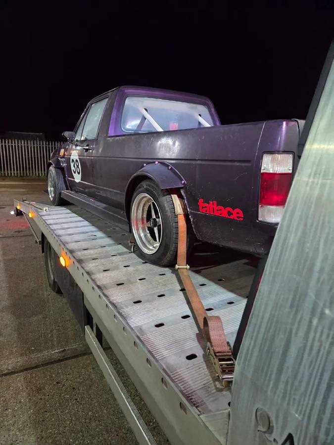 Dark vintage pickup truck secured on recovery flatbed at night location