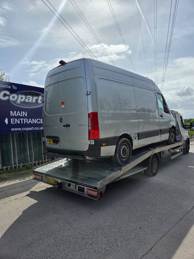 Silver Mercedes Sprinter van on flatbed by Copart vehicle auction facility